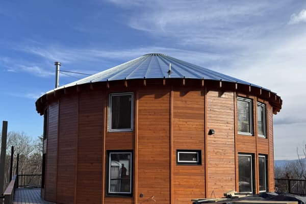 The finished wood siding and standing seam metal roof from the deck, black window frames, a stove flue, blue sky