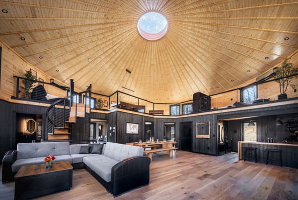 The open main room: dark lower walls, a pale wood ceiling rising to the dome, the loft with a spiral stair, a sofa, a long table and the kitchen